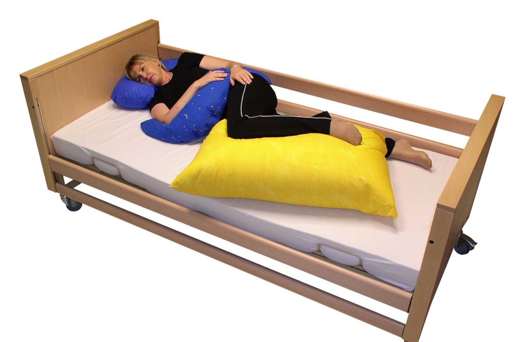 Beispiel für eine Bobath-Lagerung einer Frau in einem Bett mittels Halbmondkissen, Beinkissen und kleines Entspannungskissen
