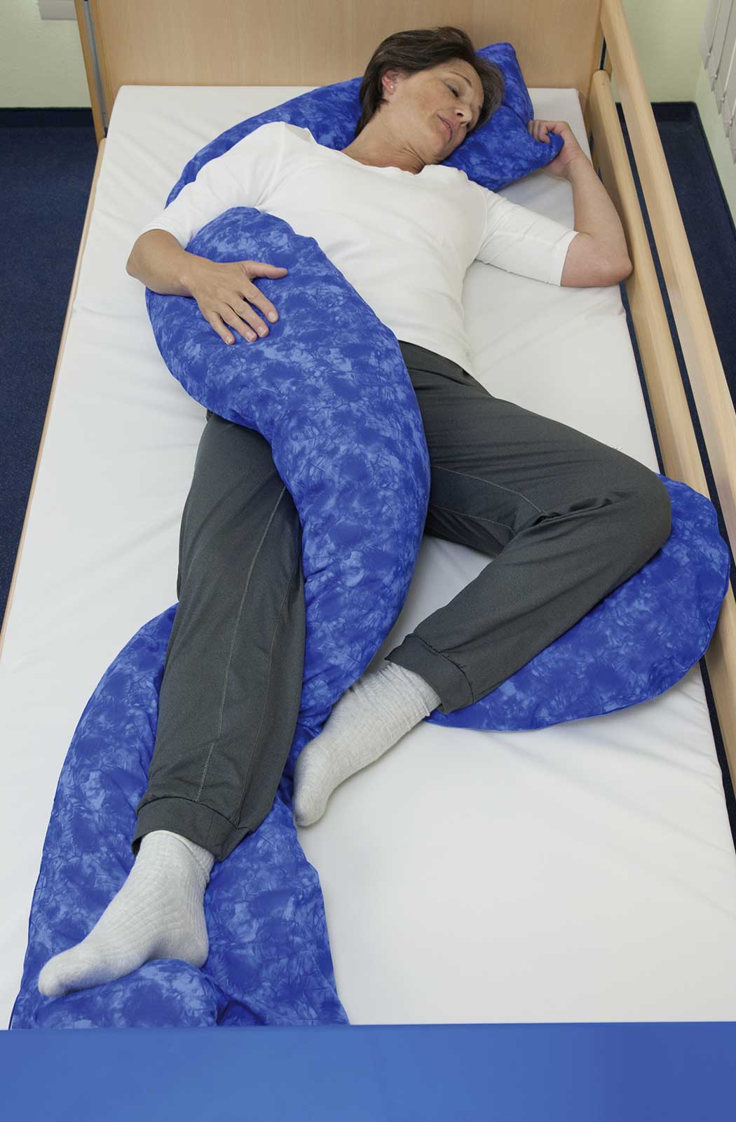 Patienten-Positionierung in S-Form: Frau liegt entspannt schlafend in einem ca. 35 cm breiten und ca. 250 cm langen Lagerungskissen in Schlangenform.