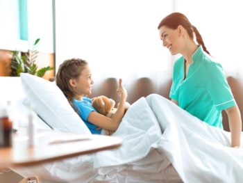 Kategoriebild Kinder - Mädchen im Krankenbett mit Krankenschwester, die auf dem Bett sitzt